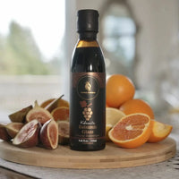 Bottle of Kalamata Balsamic Glaze on a wooden board with fruits in a bright setting