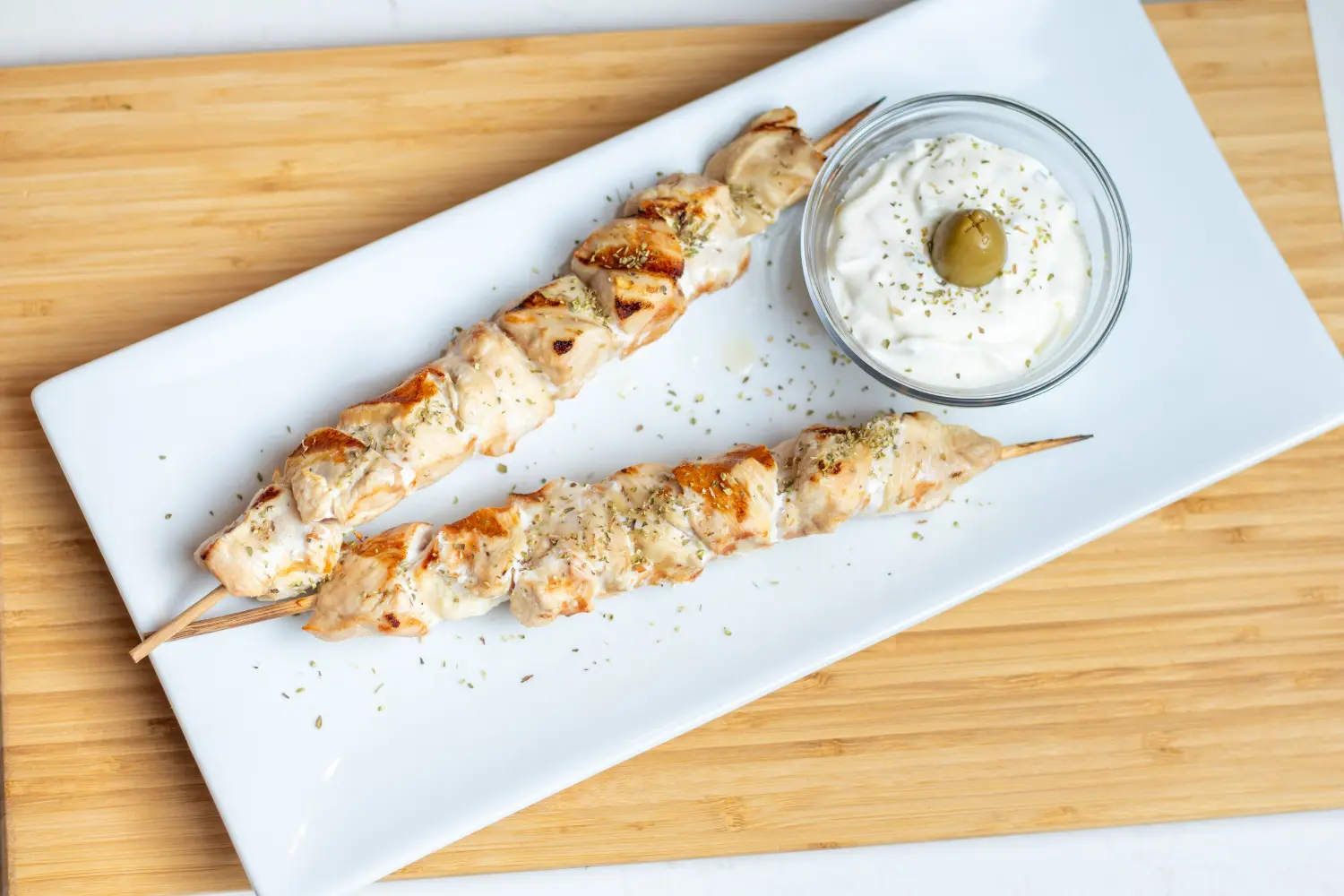 A white plate topped with two chicken skewers.