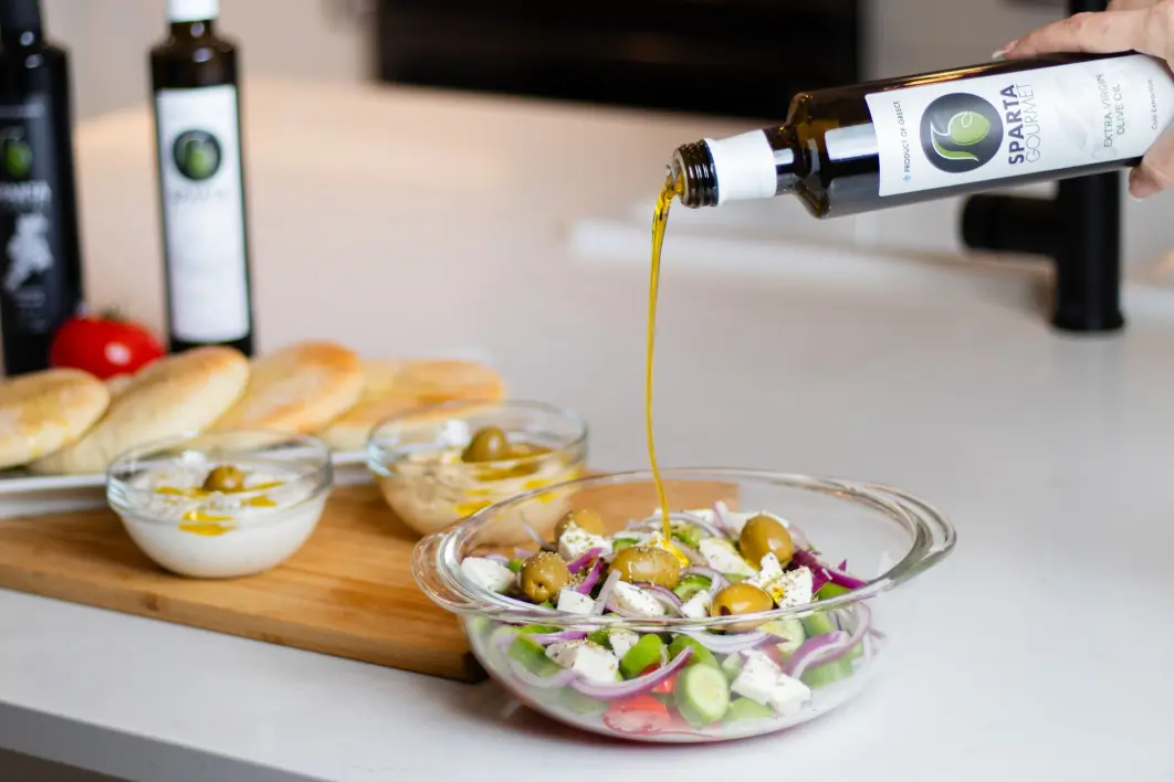 A person pouring olive oil on top of salad.