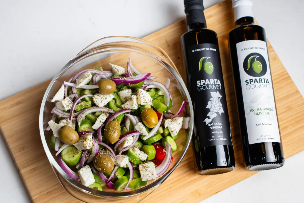 A bowl of salad next to two bottles of olive oil.